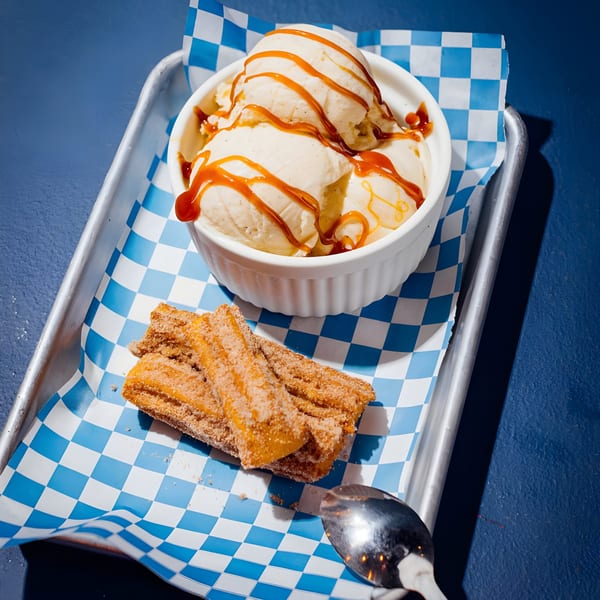 Vanilla ice cream with caramel drizzle and churros on a blue and white checkered paper liner.