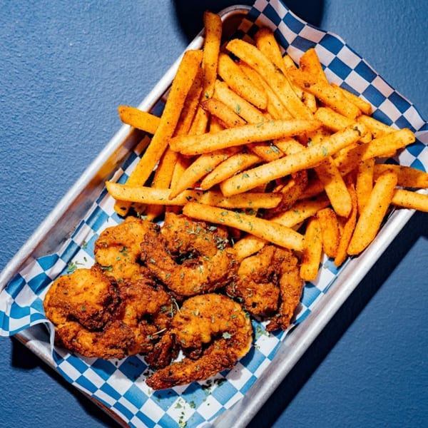 A metal tray with Shark Boy Fish and Chips' fried shrimp and seasoned french fries on blue and white checkered paper.